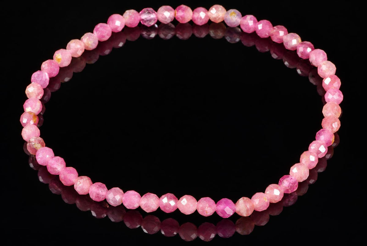 A bracelet of faceted pink beads in varying shades, arranged in a circle on a dark reflective surface.