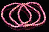 Three faceted pink beads arranged in loops on a dark reflective surface.