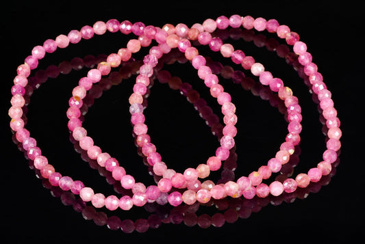 Three faceted pink beads arranged in loops on a dark reflective surface.