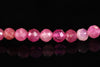 A row of faceted pink beads, varying in shade from pale to deep magenta, arranged on a dark reflective surface.