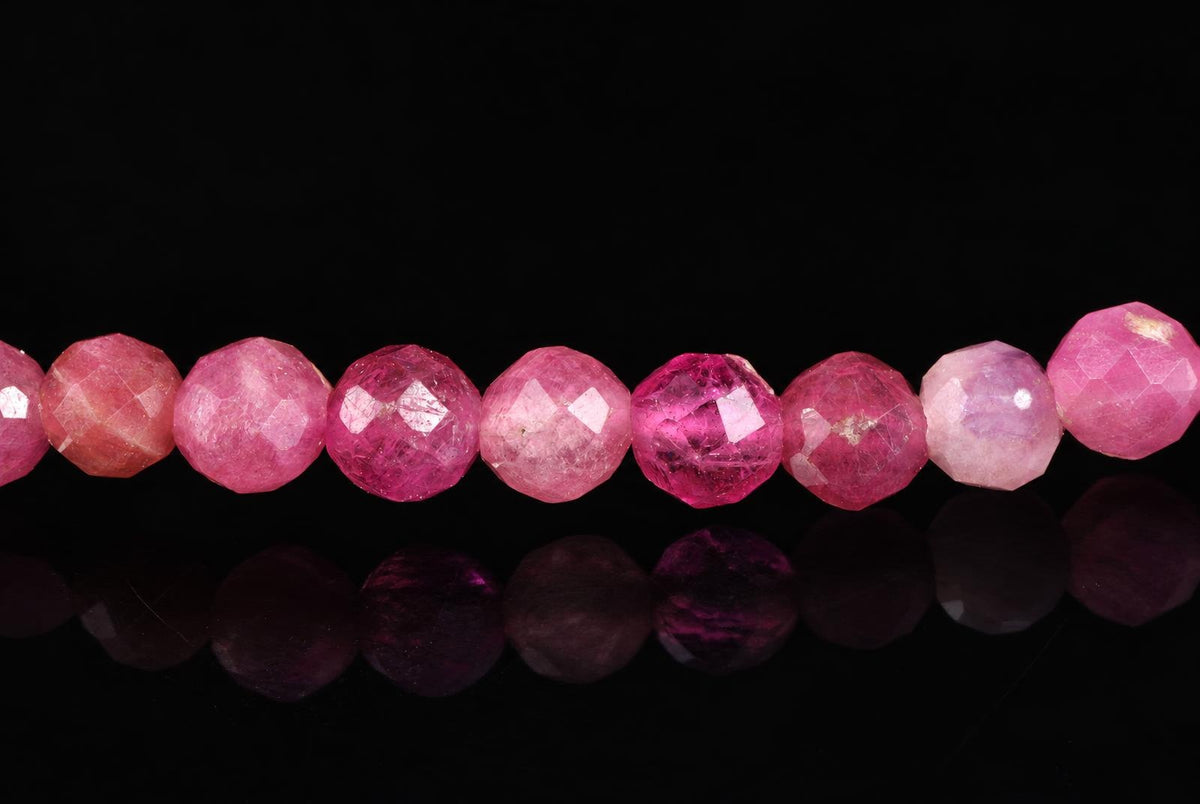 A row of faceted pink beads, varying in shade from pale to deep magenta, arranged on a dark reflective surface.