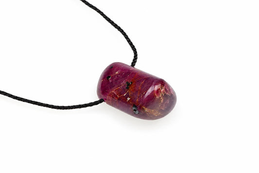 A polished, dark red ruby pendant with golden inclusions hangs from a black cord against a white background.