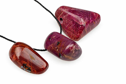 Three polished red and brown stone pendants on black cords, arranged diagonally on a white surface.