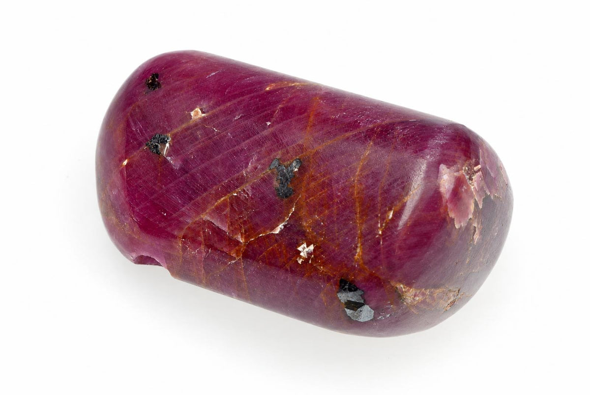 A polished, dark red stone with golden veins and small black inclusions rests on a white surface.