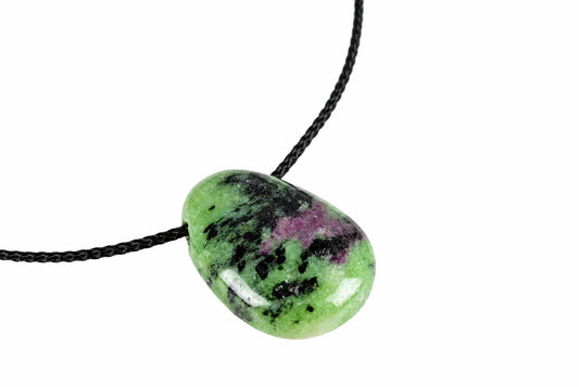 A polished green pendant with black and purple inclusions hangs from a black cord against a white background.