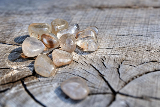A cluster of smooth, translucent Rutile quartz stones with brown inclusions rests on a weathered wooden surface.