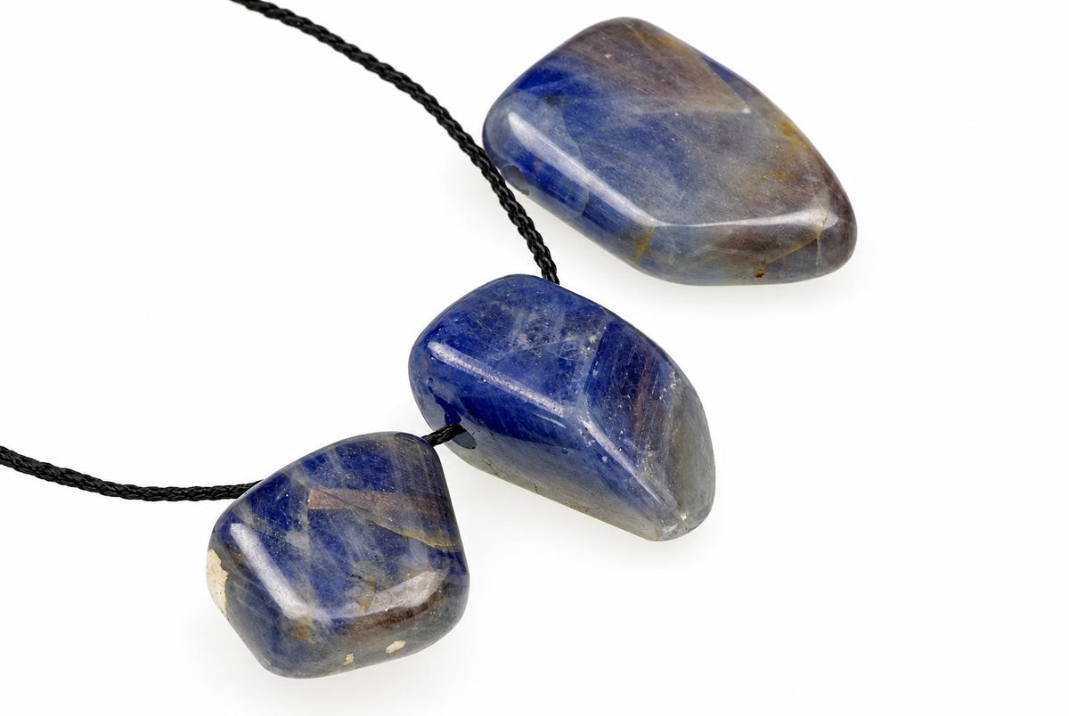 A black cord necklace with three polished, irregular blue stones on a white surface.