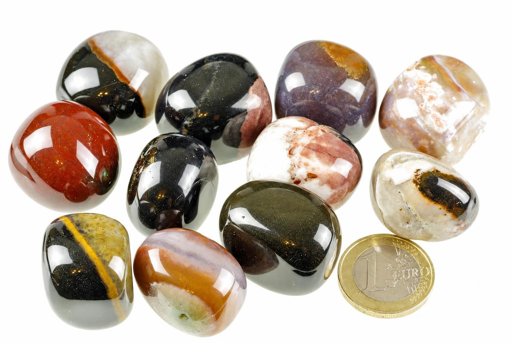 A collection of polished, multi-coloured sardonyx stones on a white surface with a one euro coin for scale.