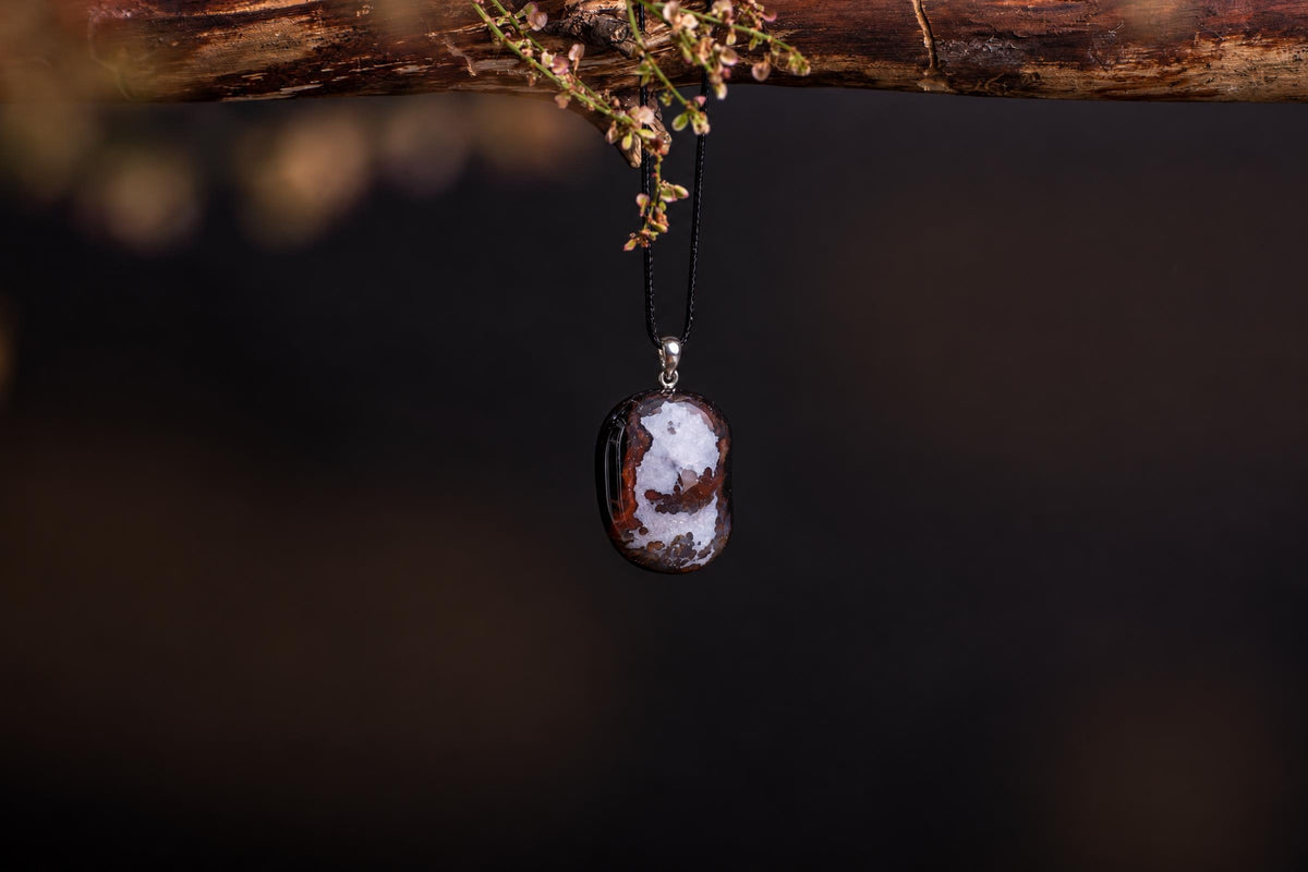 A polished sardonyx pendant with brown and white bands hangs from a black cord on a dark surface.