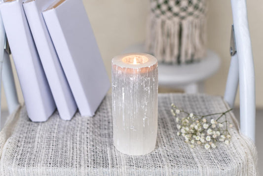 A lit candle inside a translucent, vertically striated white holder sits on a pale woven surface.