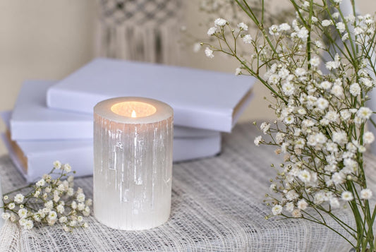 A lit candle inside a translucent, white, cylindrical holder with vertical striations sits on a pale woven surface.