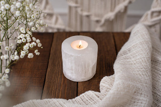 A lit candle inside a translucent, cylindrical selenite holder rests on a dark wooden surface.