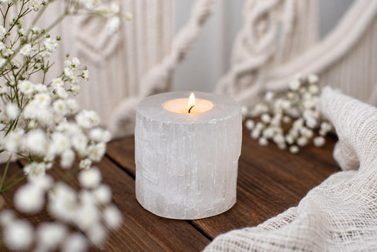 A lit candle inside a translucent, cylindrical selenite holder rests on a dark wooden surface.