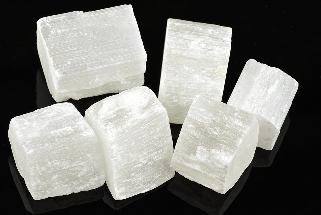 Five white selenite cubes with visible striations arranged on a dark reflective surface.