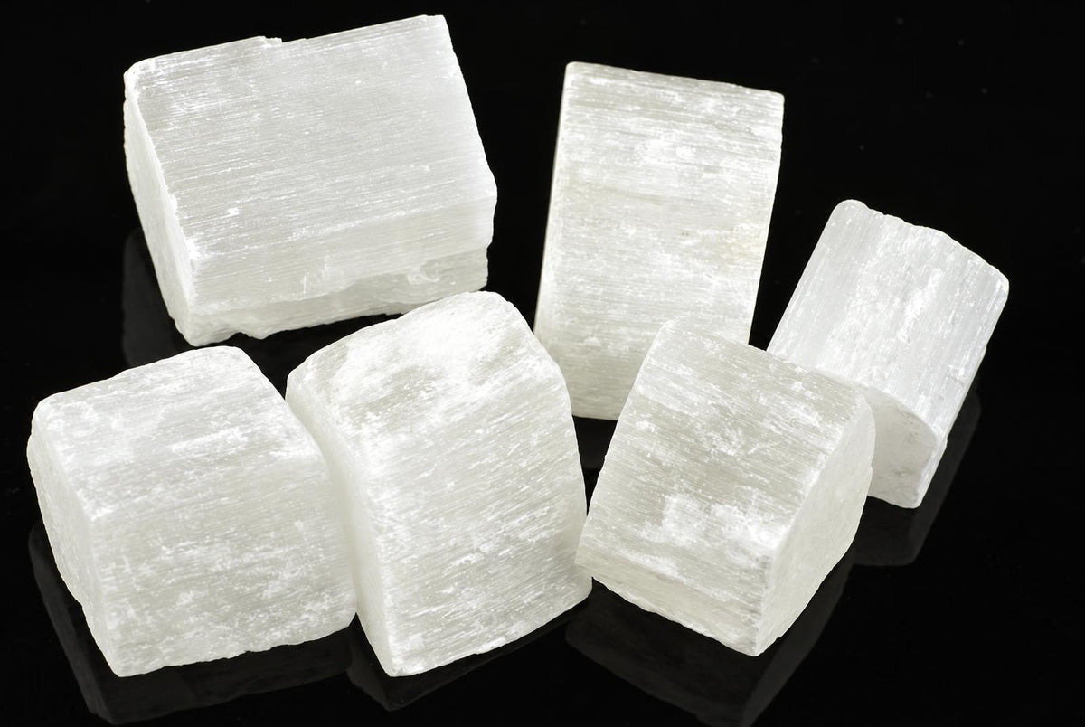 Five white selenite cubes with visible striations arranged on a dark reflective surface.