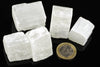 Five white selenite cubes with visible striations on a dark surface, next to a one-euro coin for scale.