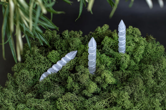 Three translucent, spiral-cut massage sticks rest on a bed of green moss with blurred foliage above.
