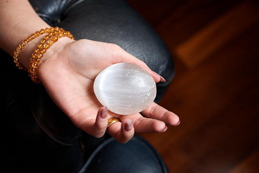A hand holds a smooth, oval-shaped white stone with visible striations against a dark surface.