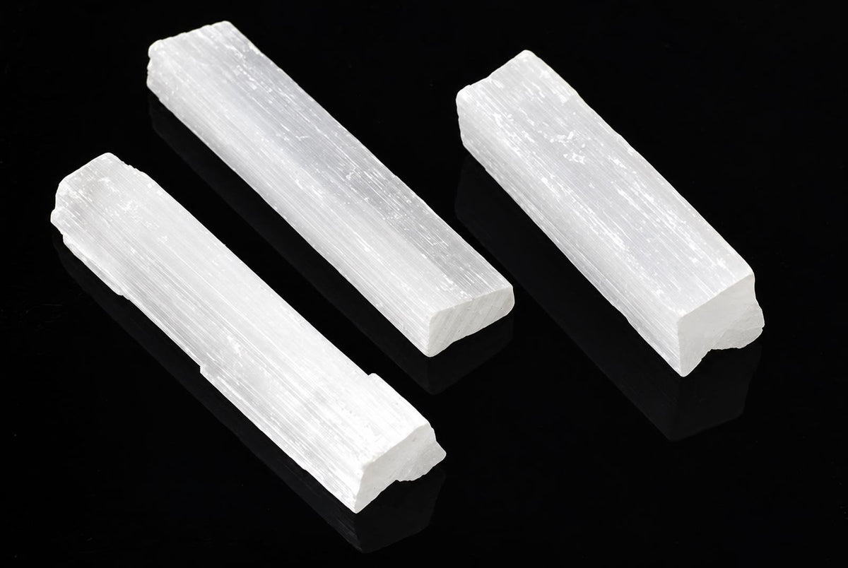 Three white, rectangular selenite sticks with a fibrous texture rest on a dark surface.