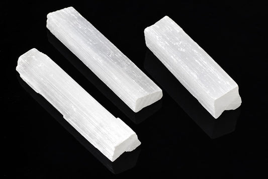 Three white, rectangular selenite sticks with a fibrous texture rest on a dark surface.
