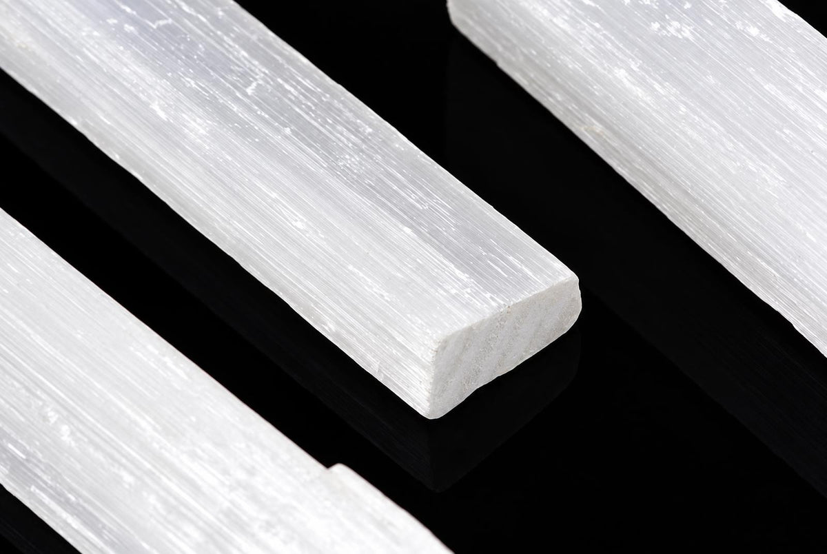 Three white selenite sticks with a fibrous texture lie on a dark surface.