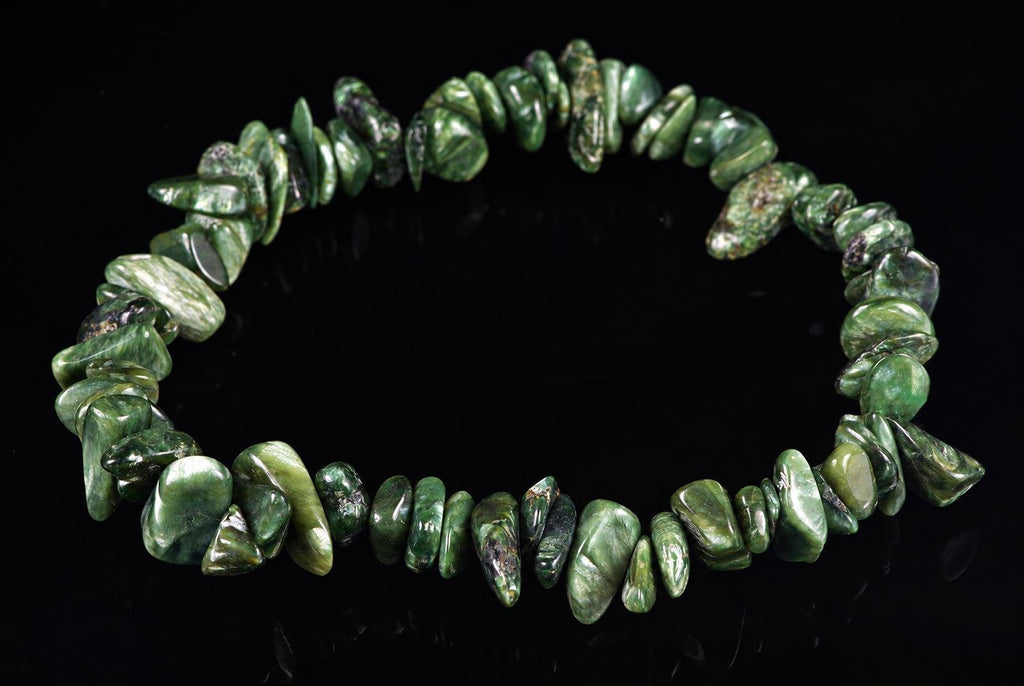 A bracelet made of irregular green chips with dark and lighter tones, arranged in a circle on a black surface.