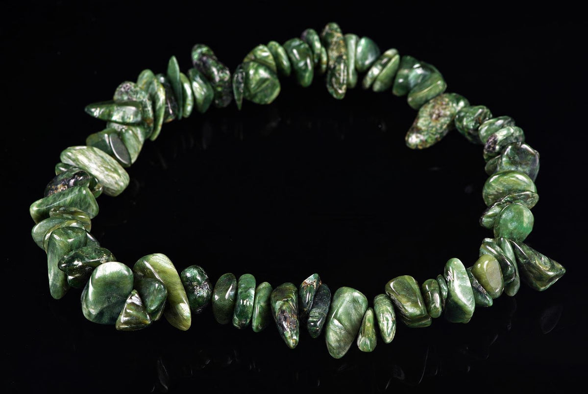 A bracelet made of irregular green chips with dark and lighter tones, arranged in a circle on a black surface.