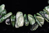 A bracelet of polished, irregular green chips with white veining arranged on a dark surface.
