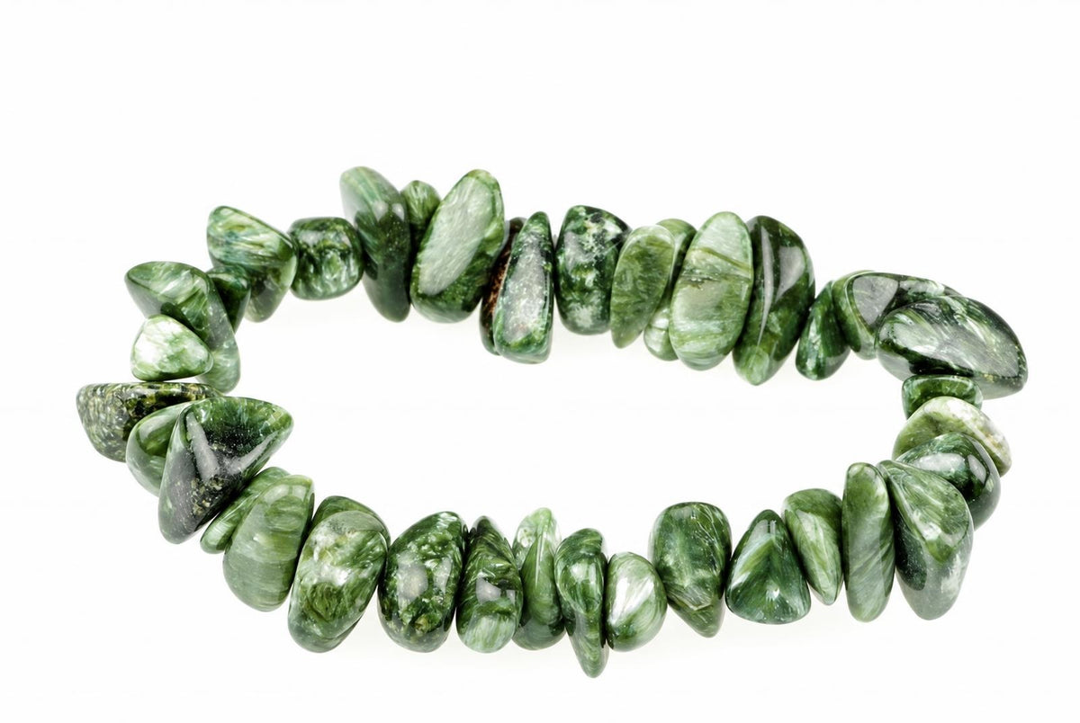 A bracelet made of polished, irregular green stones with white and dark inclusions, arranged on a pale surface.