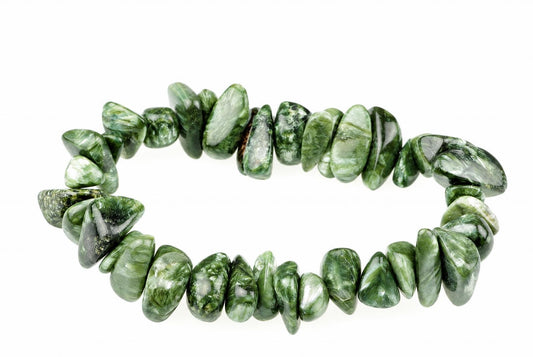 A bracelet made of polished, irregular green stones with white and dark inclusions, arranged on a pale surface.