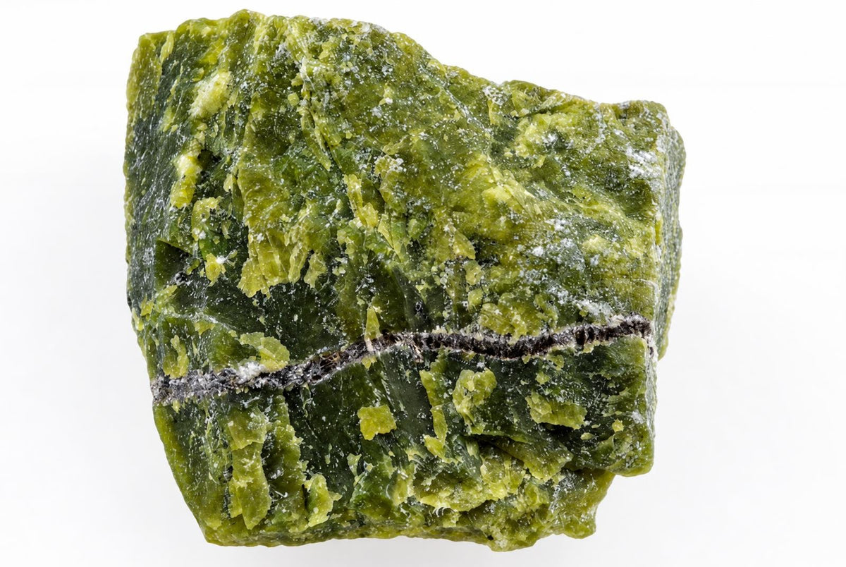 A raw piece of green serpentine mineral with a dark horizontal vein and white specks on a pale surface.