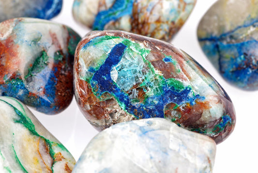 A close-up of several polished Shattuckite stones with vibrant blue, green and brown patterns on a pale surface.
