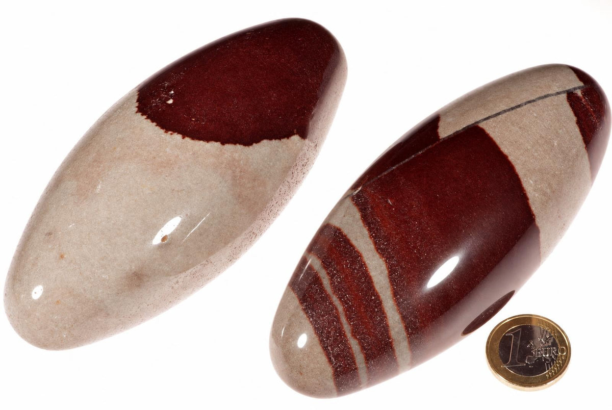 Two polished, oval-shaped stones with cream and dark red bands on a white background, next to a one-euro coin.