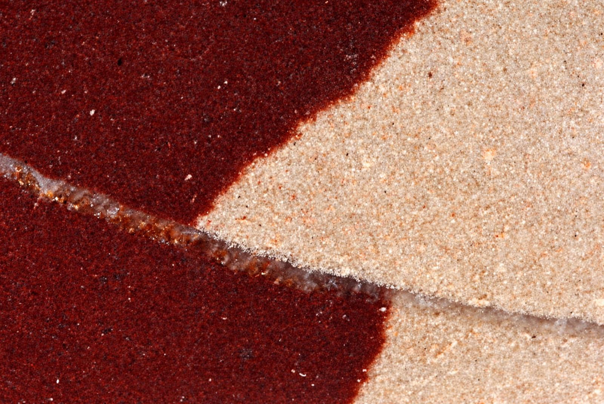 A close-up of a polished stone surface with dark red and light beige sections separated by a thin, irregular line.