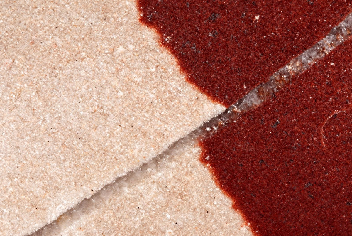A polished stone object with a light beige section and a dark red section, separated by a clear diagonal line.