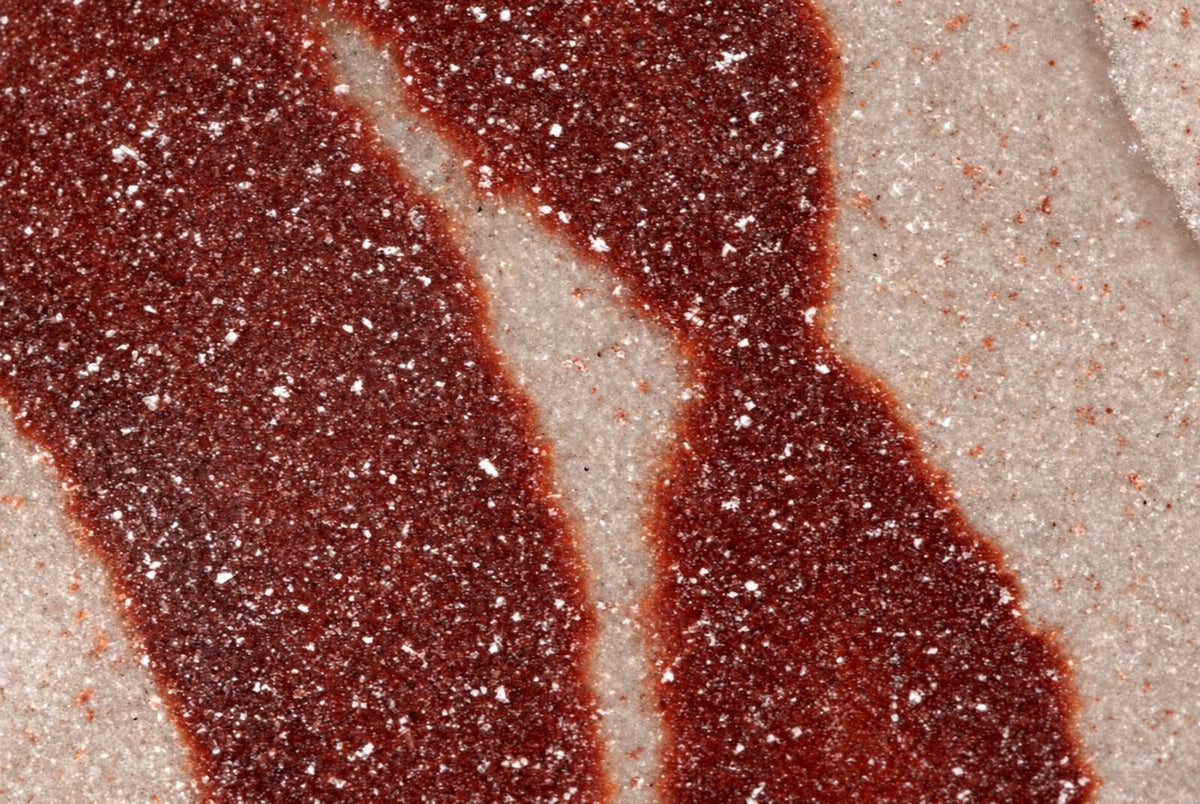 A close-up of a dark red, polished surface with white speckles on a pale background.
