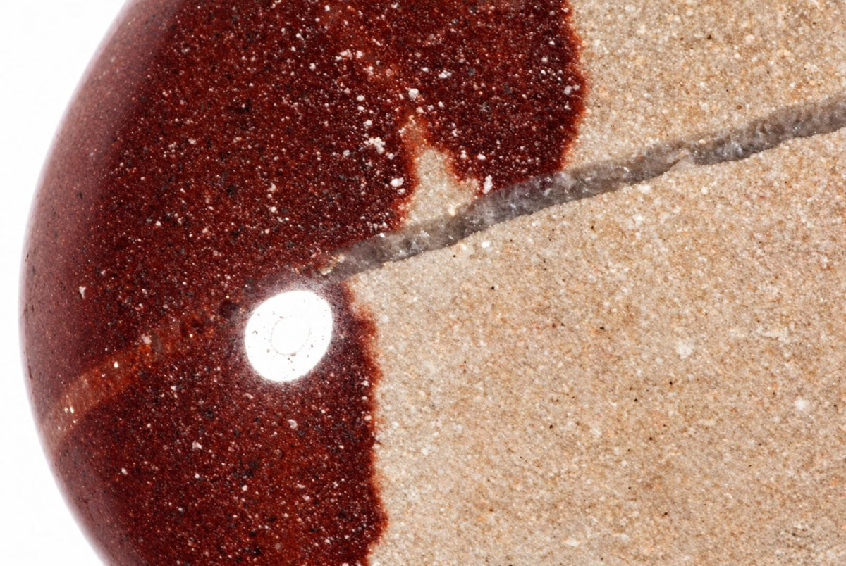 A polished stone object with a dark reddish-brown speckled section and a light beige sandy section, separated by a diagonal line.
