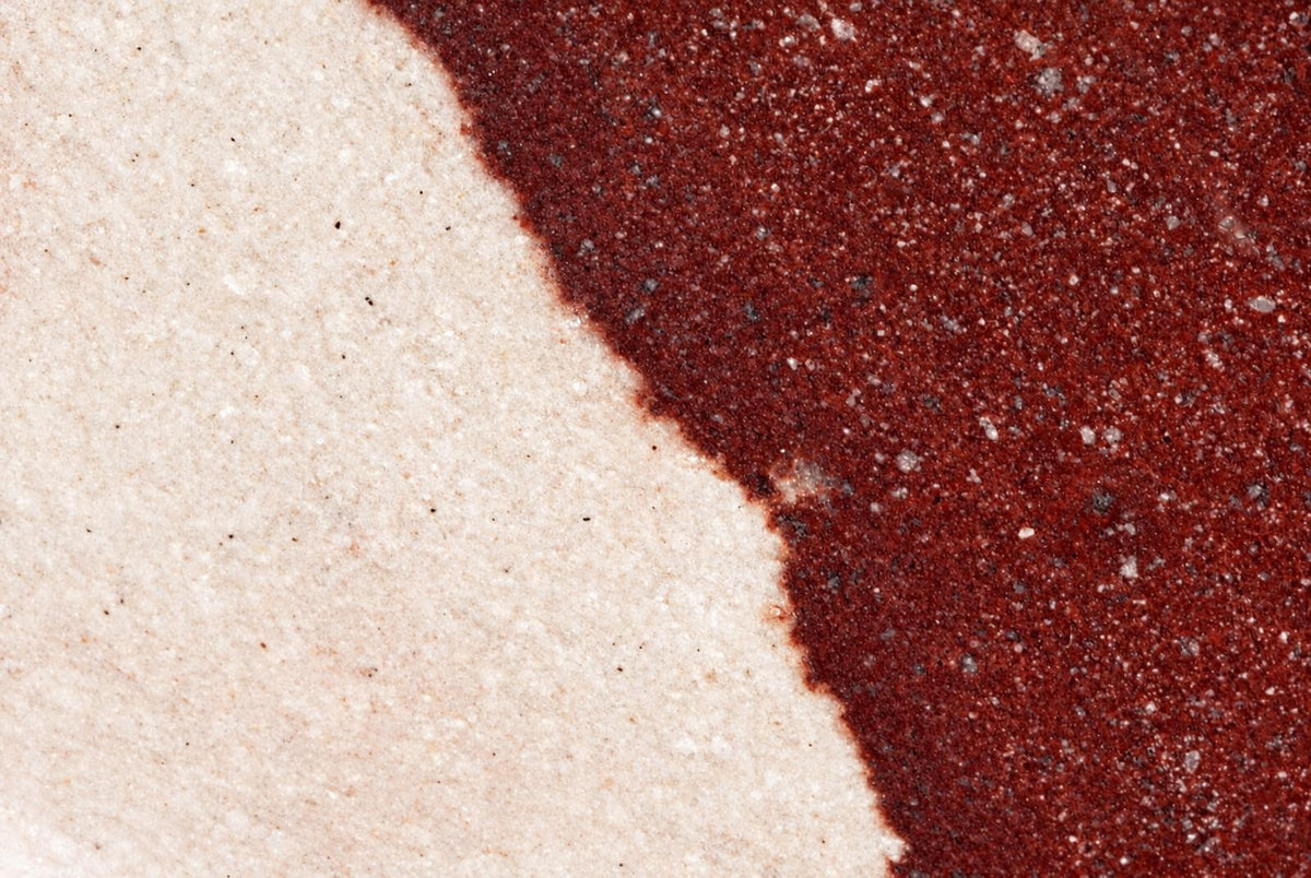 A close-up of a polished stone surface split diagonally between pale cream and dark red sections with small speckles.