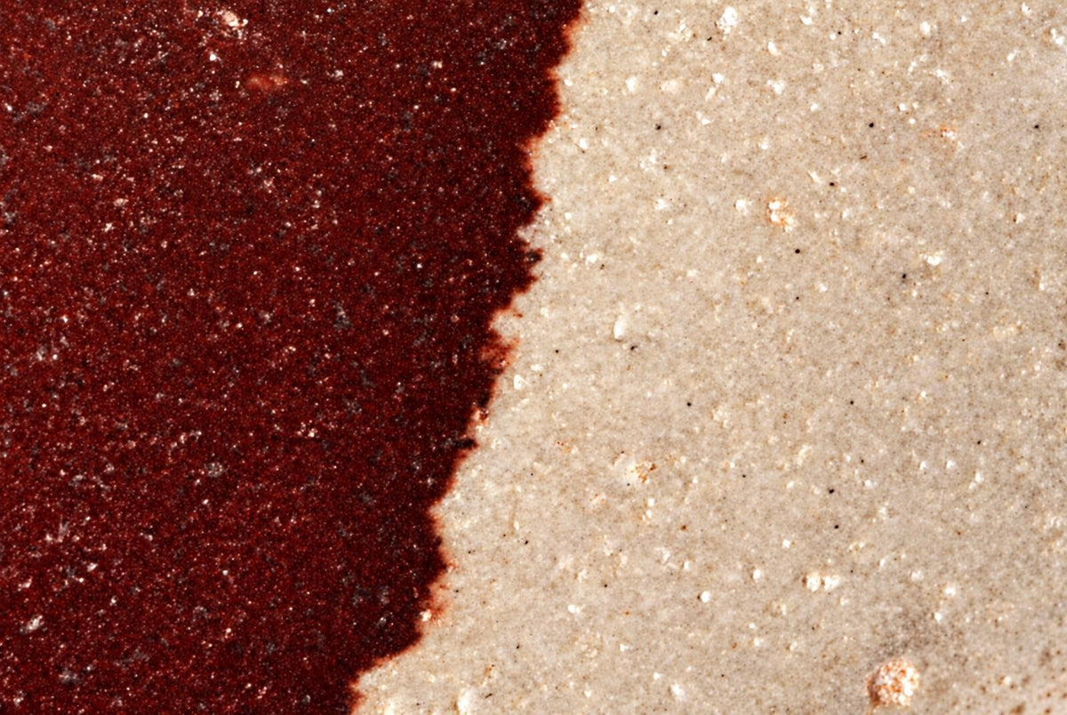 A polished stone object with a dark red left side and pale beige right side, separated by an irregular boundary.