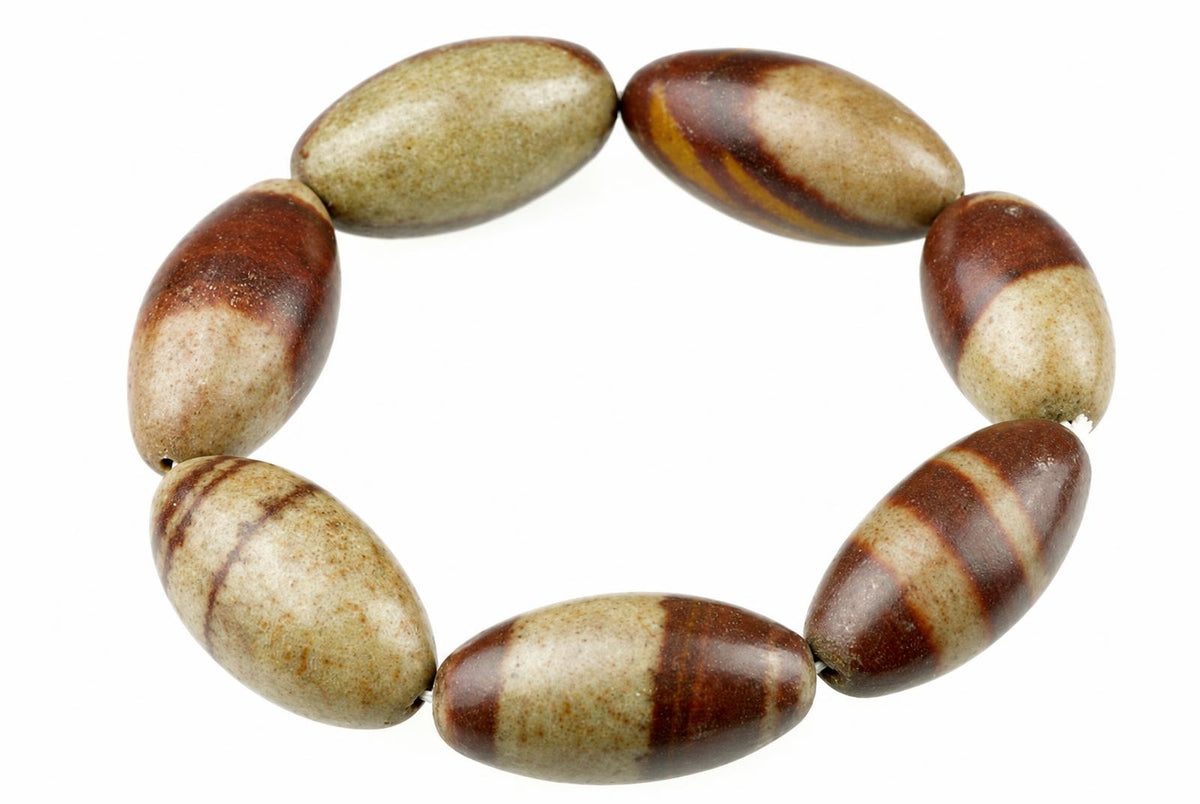 A bracelet with oval beads in dark brown and beige tones, arranged on a pale surface.