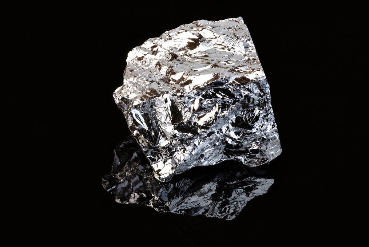 A shiny, silver-toned chunk of silicon polycrystalline sits on a dark surface with a reflection.