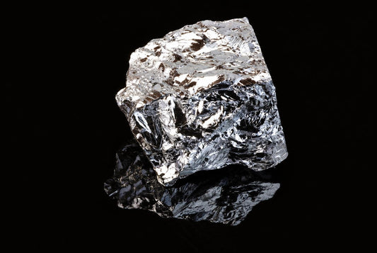 A shiny, silver-toned chunk of silicon polycrystalline sits on a dark surface with a reflection.