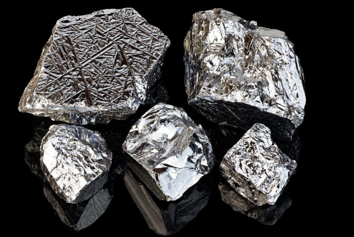 Five silver-toned, irregular silicon polycrystalline chunks with crystalline textures on a dark reflective surface.