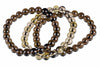 A bracelet of round, polished beads in dark brown, black and pale yellow smoke quartz on a white surface.