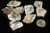 Several raw quartz crystals, mostly clear to pale yellow, on a dark surface with a one-euro coin for scale.