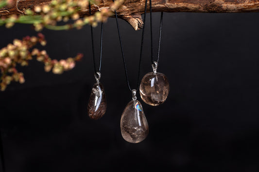 Three polished, translucent brown pendants hang from black cords on a dark surface.
