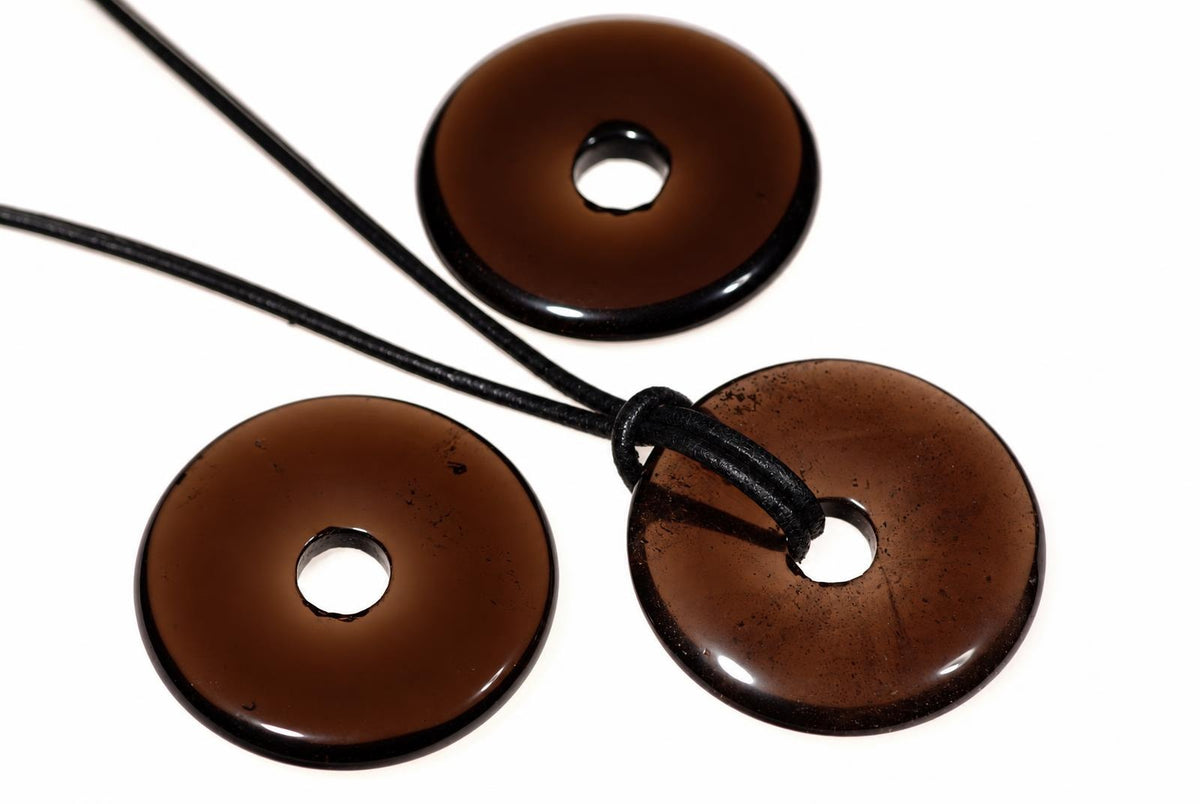 Three brown, donut-shaped pendants with central holes on black cords against a white background.