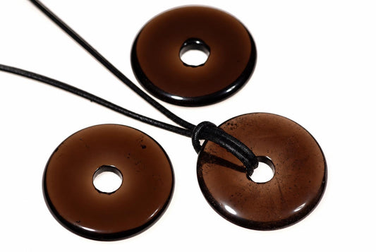 Three brown, donut-shaped pendants with central holes on black cords against a white background.