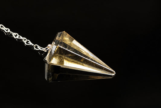 A silver-toned chain holds a faceted, translucent yellow crystal pendant shaped like a pyramid against a dark surface.