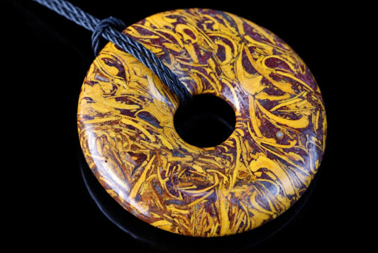 A polished, donut-shaped pendant with swirling yellow and dark red patterns on a black surface.